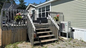 A wooden deck with outdoor furniture, a set of wooden stairs, and a house with a grey siding exterior. - Coastal Trail Getaway (Port Hood)