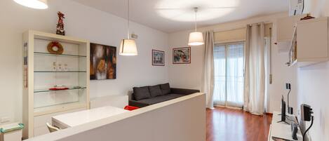 Una sala de estar moderna con un sofá, un aparador de vidrio con adornos, y un comedor con una mesa y sillas blancas.