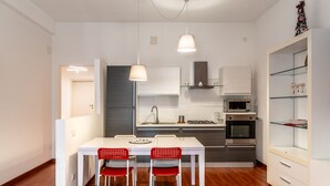 A compact kitchen with white cabinets, a microwave, an oven, and a dining area with a white table and red chairs. - Bacchilide Novanta by Wonderful Italy (Syracuse)