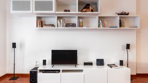 A modern living room with a flat-screen TV, white entertainment unit, and built-in shelves with books and decorative items. - Bacchilide Novanta by Wonderful Italy (Syracuse)