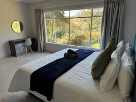 Un dormitorio con un ventanal grande, una cama con almohadas, una colcha azul, un escritorio y una silla.