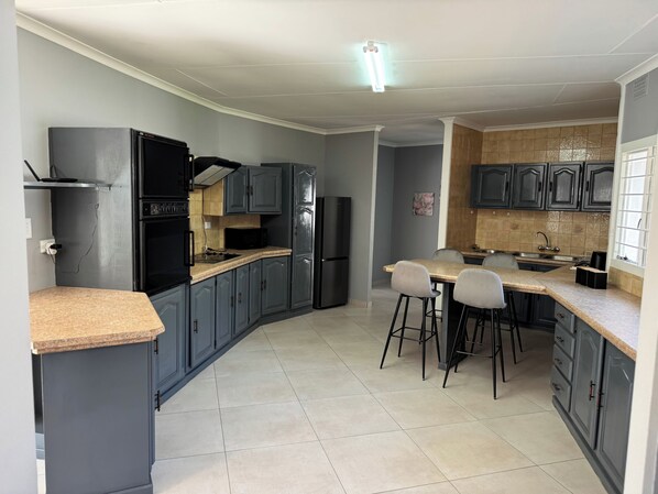 A modern kitchen with grey cabinets, a black refrigerator, a microwave, and a dining area with bar stools.