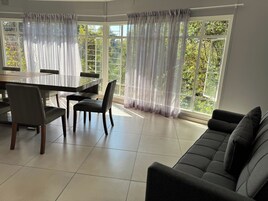 Un comedor con una mesa y sillas, un sofá y ventanas amplias con cortinas de gasa.