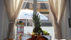 Een ontbijttafel met croissants, ham en een ananas. Er is een fles sinaasappelsap en een pak sinaasappelsap.