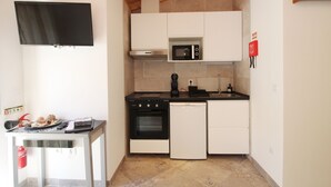 Een kleine keuken met witte kastjes, een magnetron, een oven en een vaatwasser.