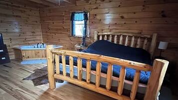 A wooden cabin room with a bed, a window, a ceiling fan, and a small table.