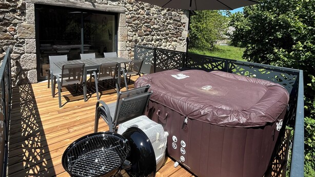 Edificio de piedra con terraza de madera, mobiliario exterior, jacuzzi y parrilla.