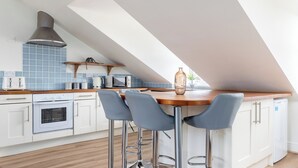 A modern kitchen with white cabinets, a wooden countertop, and a built-in oven. There are three bar stools and a large window providing natural light. - Stylish Flat in Wandsworth (London)