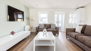 A modern living room with a white coffee table, two sofas, a white console table, and a large flat-screen TV mounted on the wall. - Stylish Flat in Wandsworth (London)