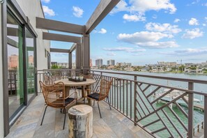 Ein Balkon mit Korbstühlen und einem Tisch, mit Blick auf einen Fluss und Gebäude im Hintergrund.
