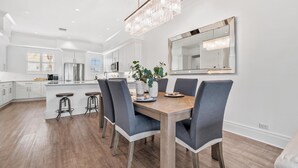 A modern kitchen with white cabinetry, a central island, bar stools, and a chandelier.