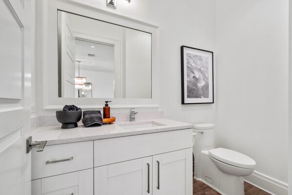 A modern bathroom with a white vanity, a large mirror, a framed artwork, and a toilet.