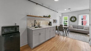A modern kitchen with a microwave, sink, and cabinets, a dining area with chairs, a sofa, and a view of greenery outside. - Downtown Boutique Comfort w/ Style- Otter Suite (Saint Charles)