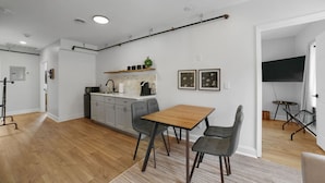 A modern kitchen with a dining area, wooden flooring, and a TV in the adjacent room. - Downtown Boutique Comfort w/ Style- Otter Suite (Saint Charles)