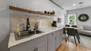 A modern kitchen with a sink, countertop, and cabinets. There is a dining area with a table and chairs. - Downtown Boutique Comfort w/ Style- Otter Suite (Saint Charles)
