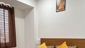 A bedroom with a bed, a wooden headboard, a nightstand, a wall-mounted painting, and a window with curtains. - Hotel Bhakti Pride Nashik (Nashik)