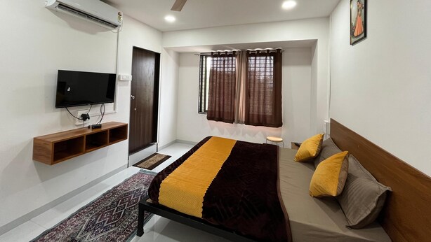 A bedroom with a bed, a television, a ceiling fan, and a window with curtains. - Hotel Bhakti Pride Nashik (Nashik)