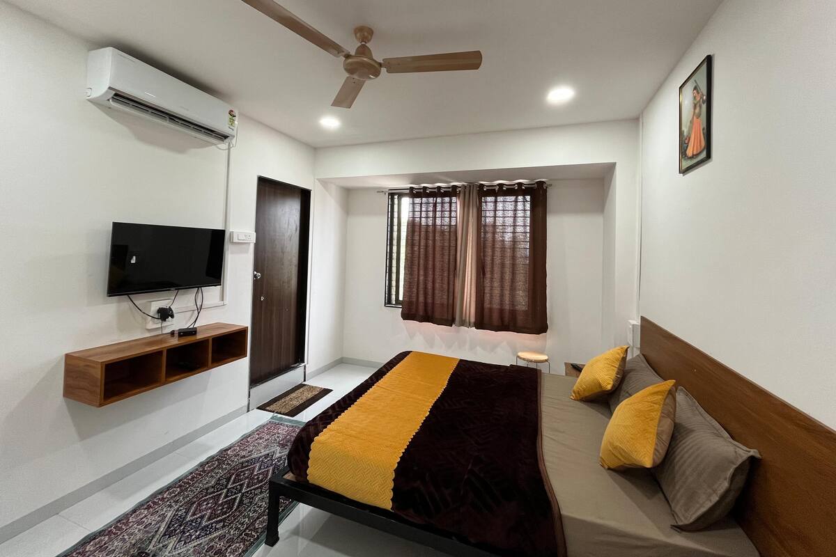 A bedroom with a bed, a television, a ceiling fan, and a window with curtains.