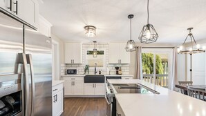 Una cocina moderna con armarios blancos, electrodomésticos de acero inoxidable e iluminación colgante.