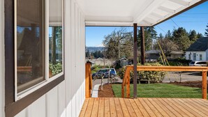 Una terraza de madera con vistas a una calle residencial y montañas al fondo.