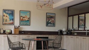 Une cuisine moderne avec un coin repas, comprenant un îlot central, deux chaises, un luminaire suspendu et trois tableaux encadrés accrochés au mur.