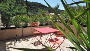 Une terrasse extérieure avec une table et des chaises rouges, entourée de plantes en pot et offrant une vue sur une colline boisée.