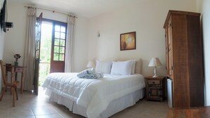 Quarto com cama, armário de madeira, escrivaninha com abajur e janela com cortinas.