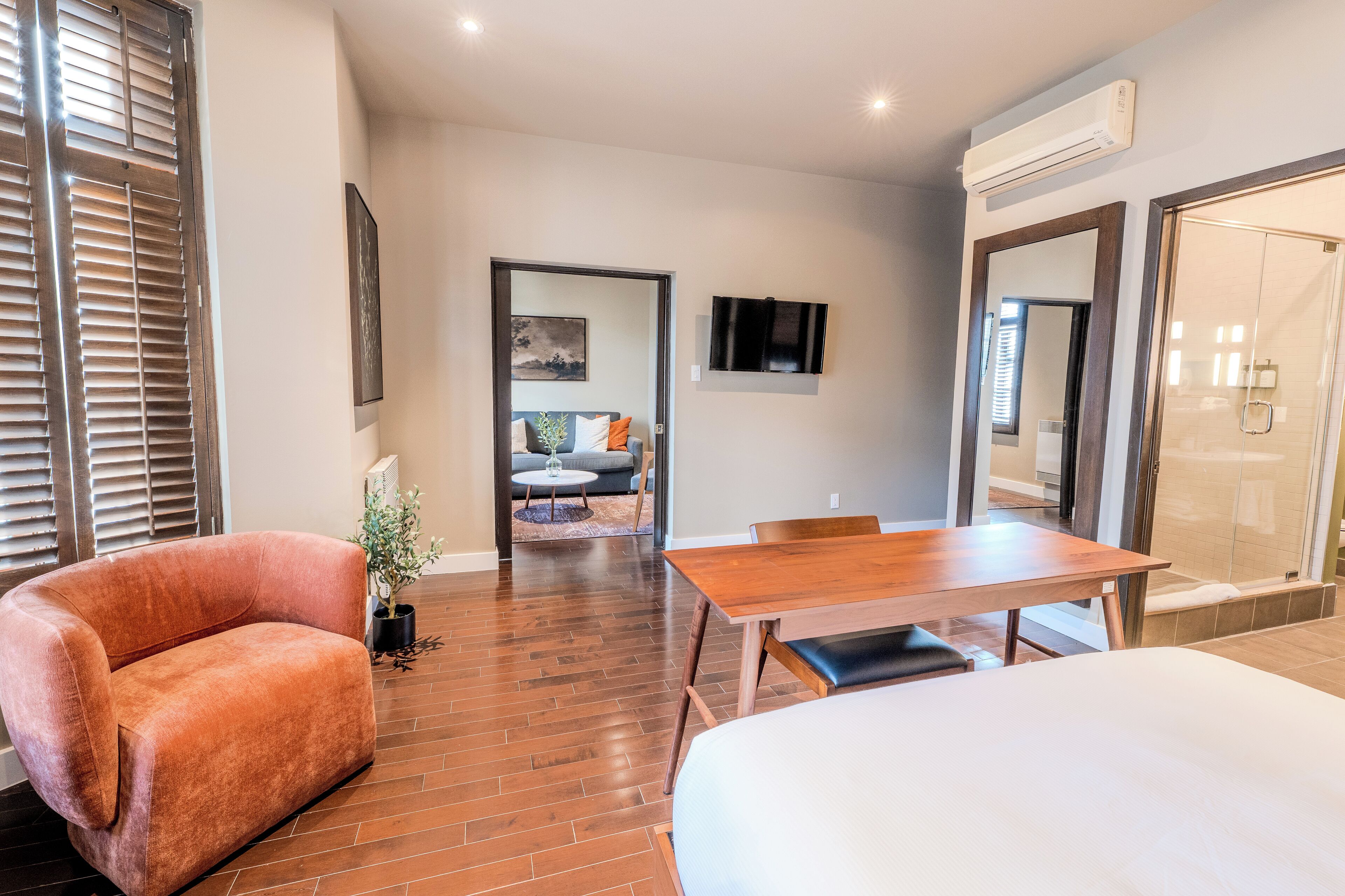A hotel room with a wooden floor, a sofa, a dining table, and a bed.