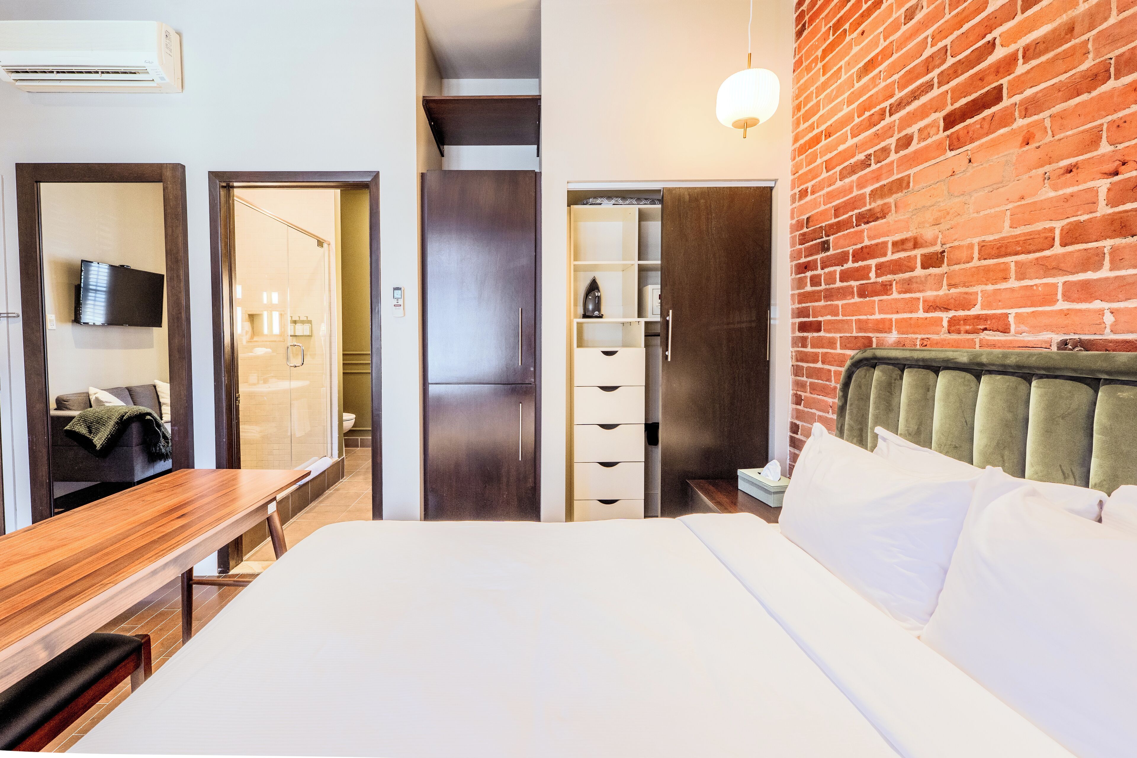 A hotel room with a bed, a wooden desk, a television, and a brick wall.
