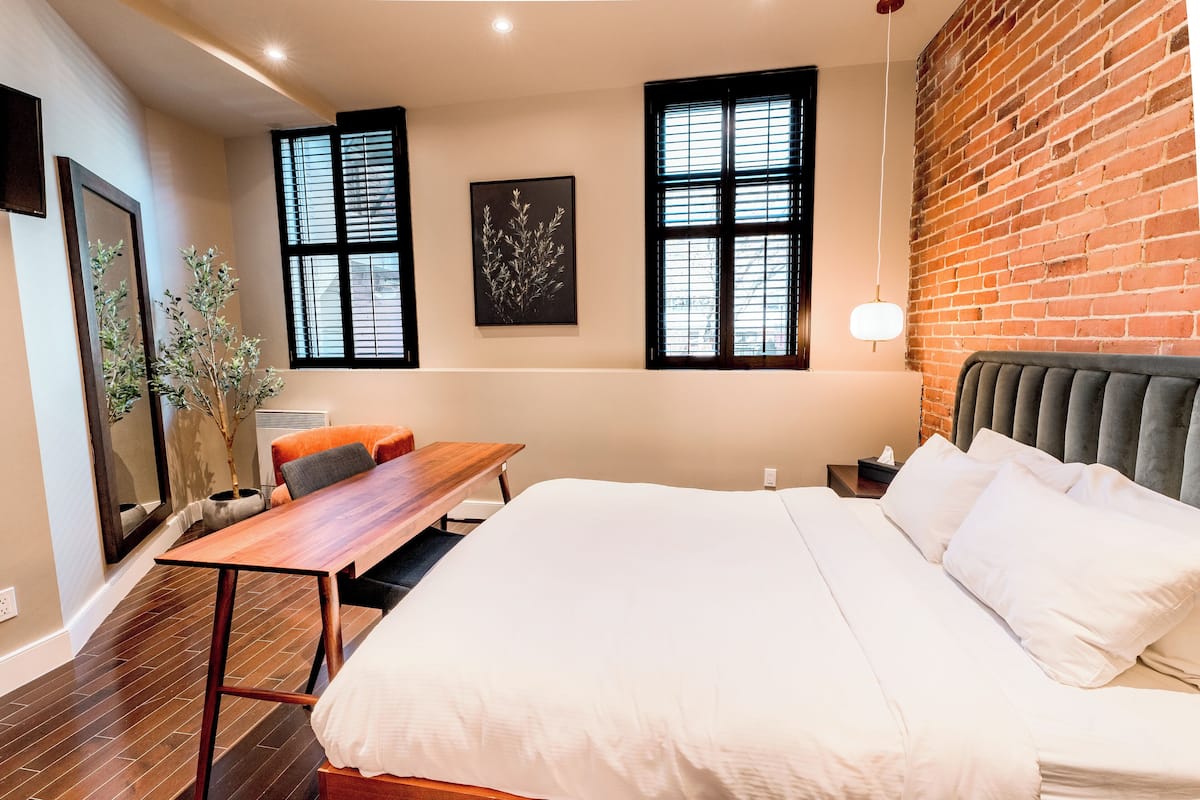 Une chambre d’hôtel avec un grand lit, un bureau en bois et deux fenêtres à cadres noirs.