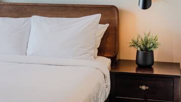 A neatly made bed with white linens, a dark wooden headboard, and a wall-mounted painting depicting a landscape.