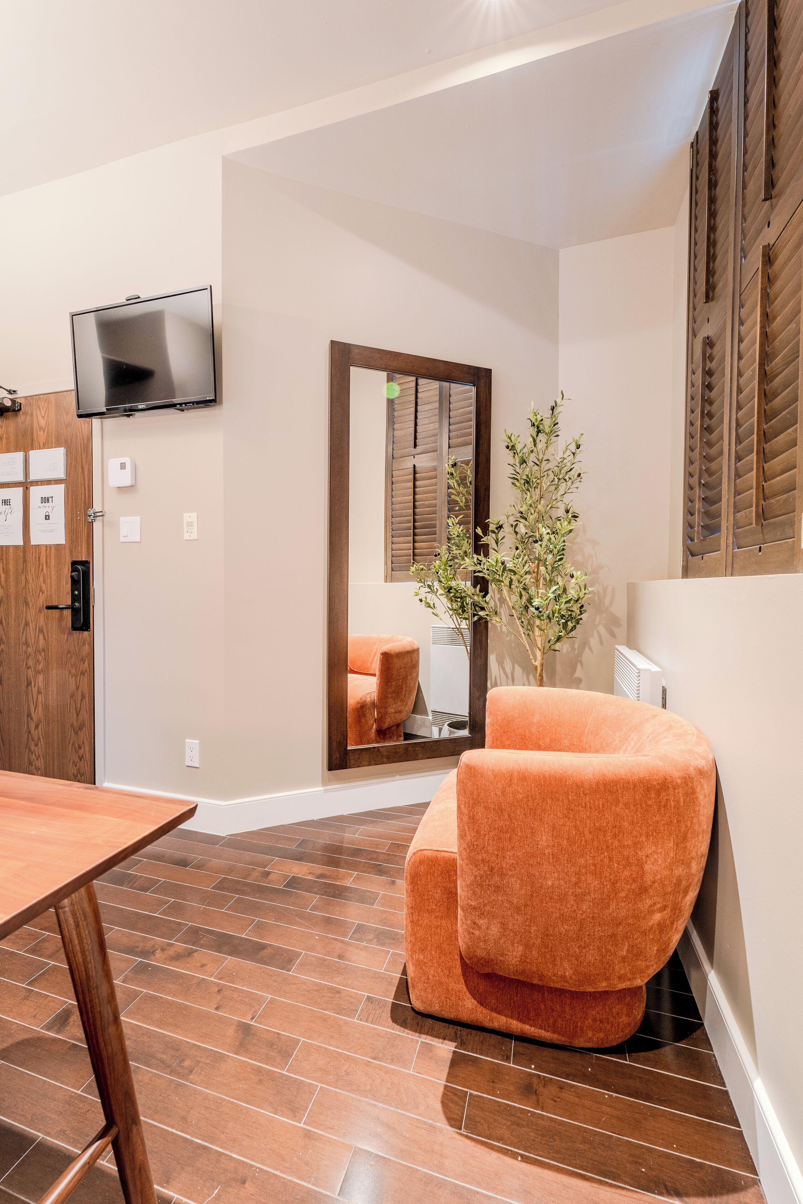 A modern room with a wooden floor, a large mirror, a television, and a comfortable orange chair.