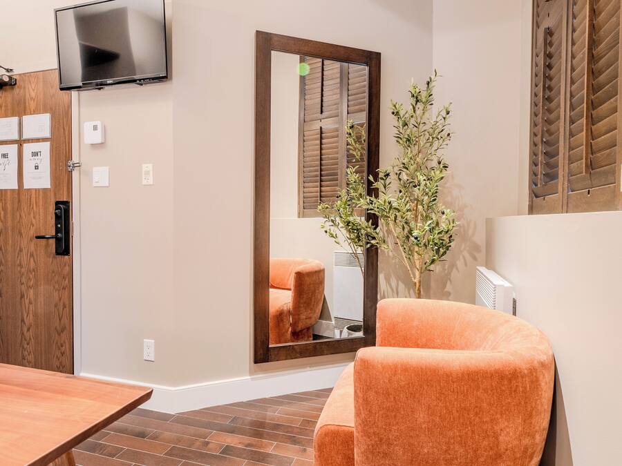 A modern room with a wooden floor, a large mirror, a television, and a comfortable orange chair.