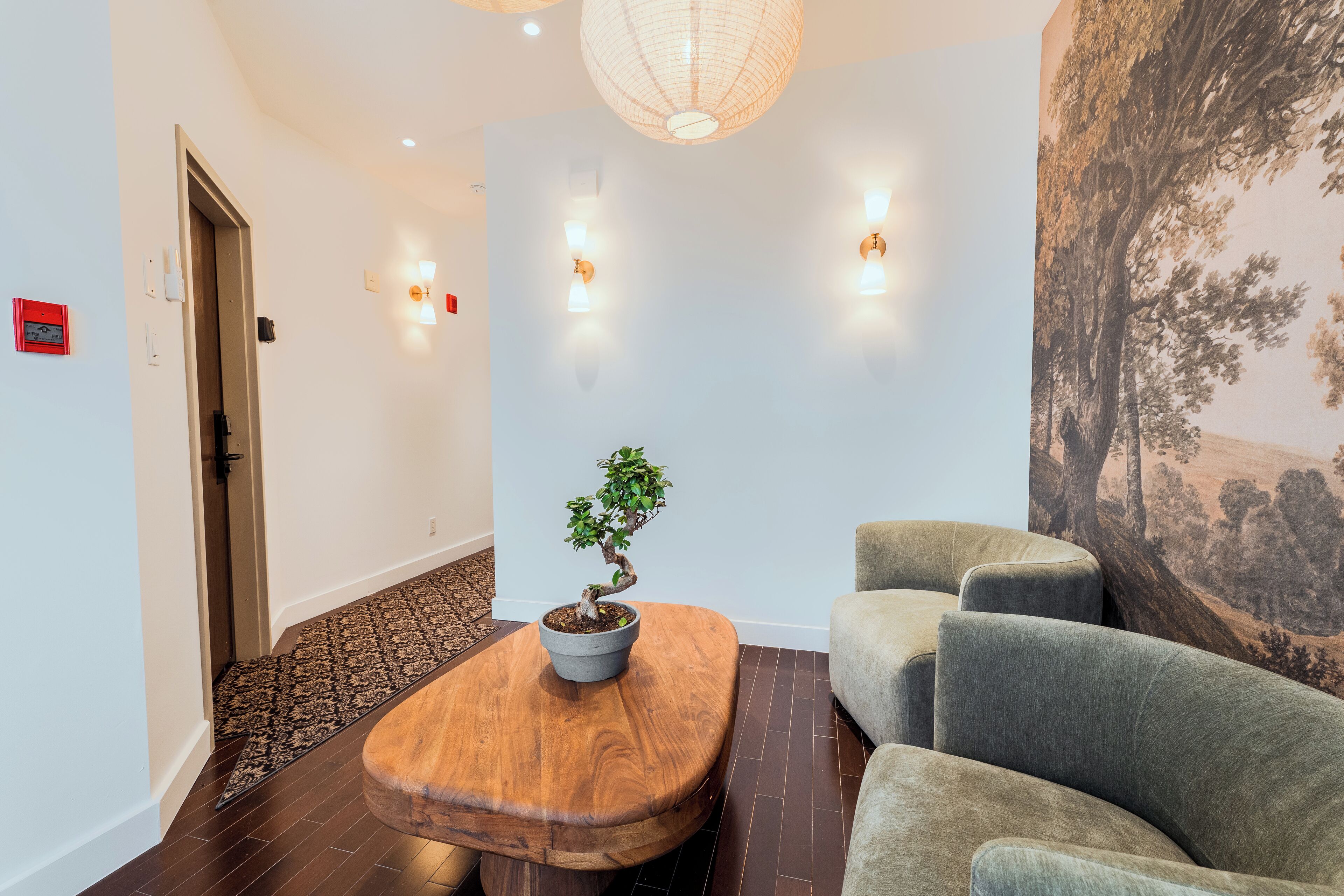 Un vestíbulo moderno con una mesa de centro de madera, una planta en maceta y una zona de estar con sofás grises.