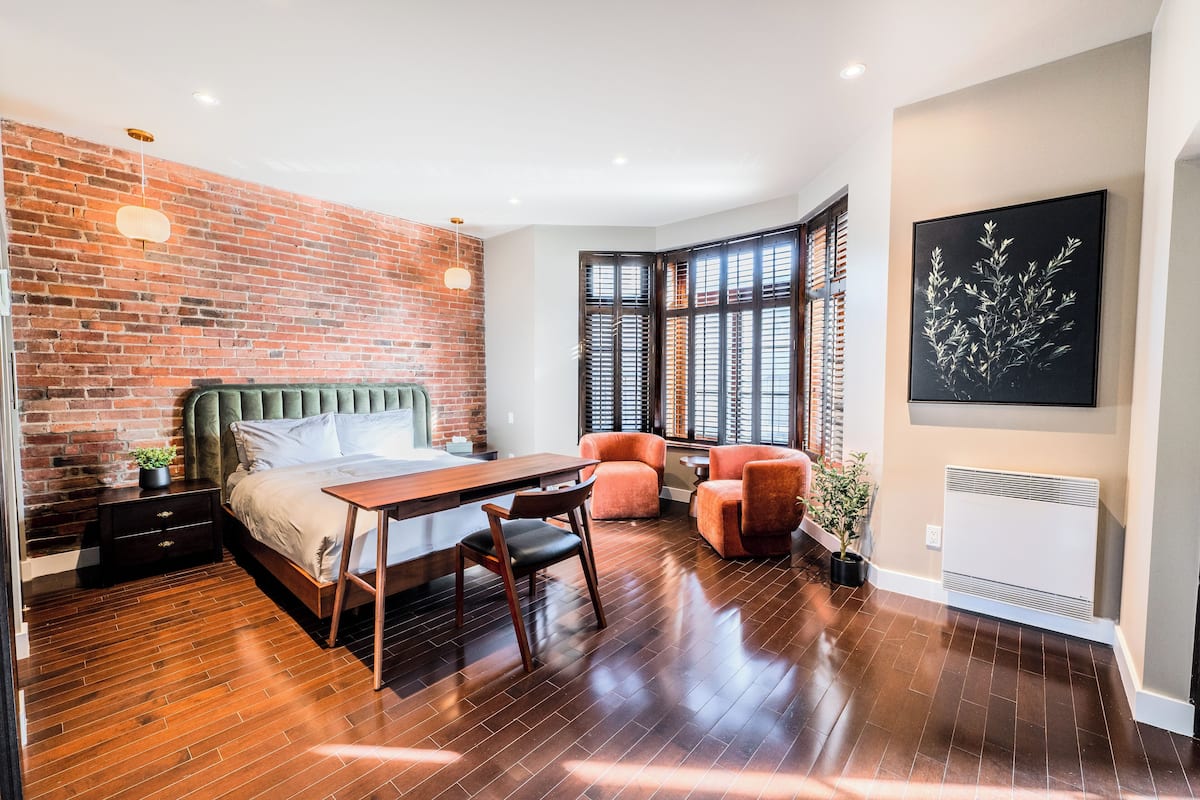 Une chambre moderne avec un mur en briques, un lit, un bureau et deux chaises.