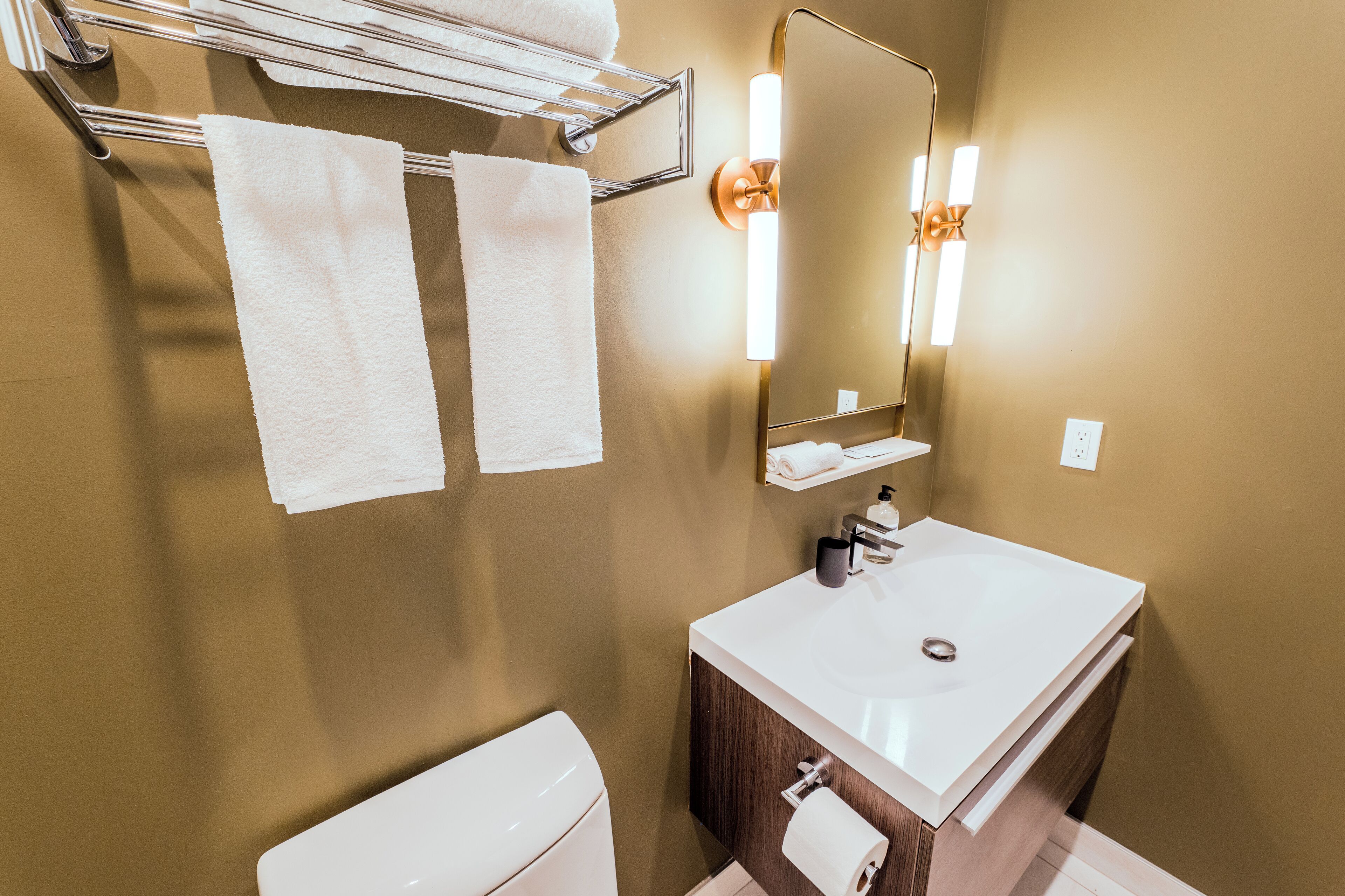 A bathroom with a white sink, a mirror, a towel rack with two towels, and a toilet.
