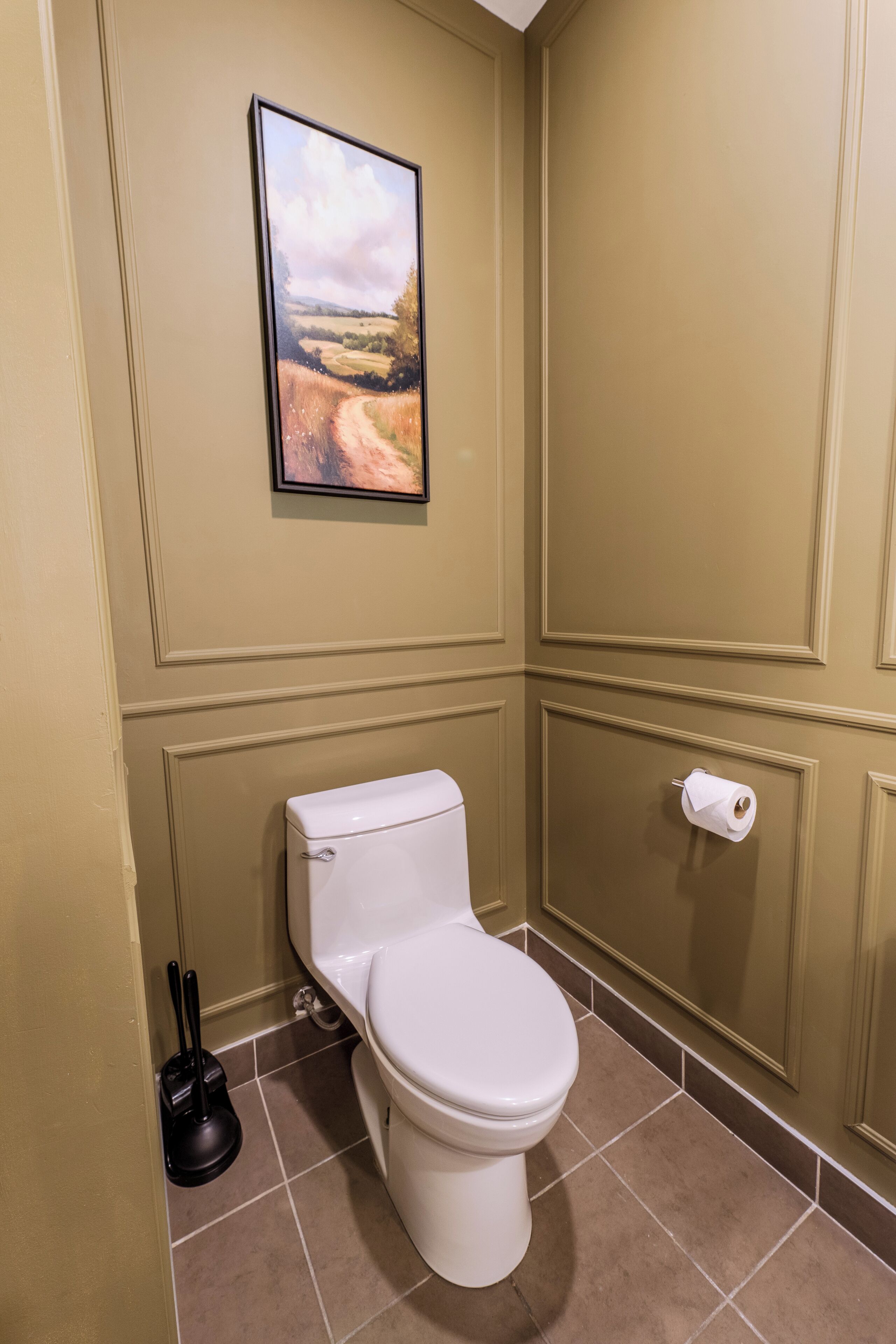 A bathroom with a toilet, a plunger, and a toilet paper holder.