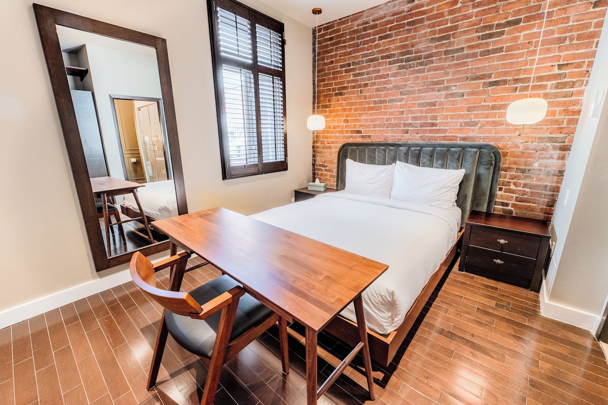 Une chambre d’hôtel moderne avec un mur en briques, un lit en bois, un bureau avec une chaise et une table de chevet.