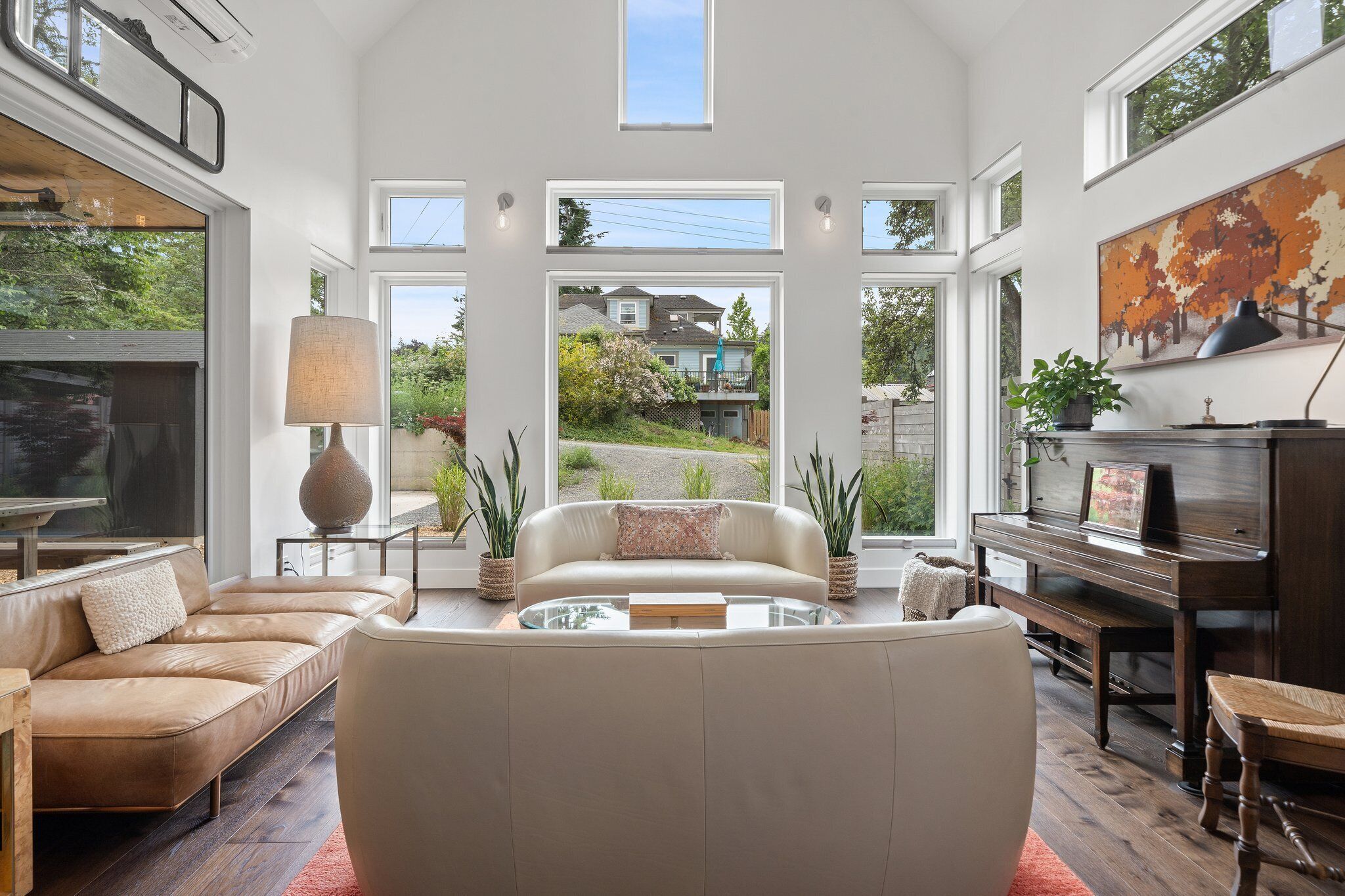 A spacious living room with a large window, a piano, and a sofa.