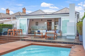 Una casa moderna con piscina, area salotto esterna e veranda in vetro.