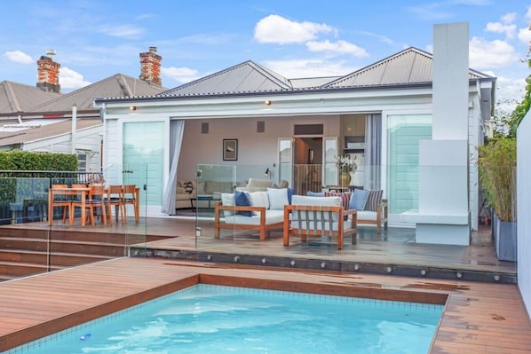 Una casa moderna con piscina, mobiliario exterior y un porche con paredes de vidrio.