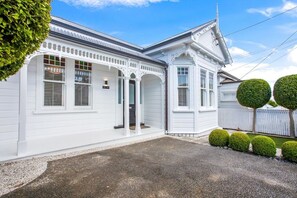 Ein weißes Gebäude mit Veranda, Garage und einem umzäunten Garten mit geschnittenen Büschen.