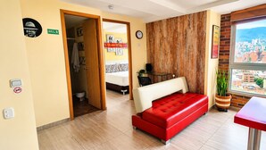 Habitación de hotel con cama, sofá rojo, pared decorativa de madera, ventana con vista a la ciudad y una mesita.