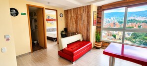 Une chambre d’hôtel avec un lit, un canapé rouge, un mur décoratif en bois, une fenêtre donnant sur la ville et une petite table.