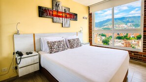 A hotel room with a bed, a nightstand, a telephone, and a large window with a city view. - Laureles elegant Spring City Treat  (Medellín)