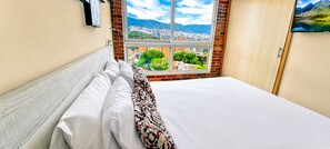 Een hotelkamer met een bed, een raam met uitzicht over de stad en een deur.