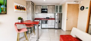 A compact kitchen with a red bar stool, a built-in oven, and a stainless steel refrigerator.