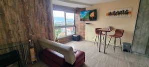 Una sala de estar con un sofá rojo, una mesita con dos sillas, un televisor y un cuadro en la pared.