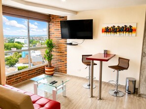 A modern living room with a large window, a flat-screen TV, a painting, a glass coffee table, and two bar stools. - Laureles elegant Spring City Treat  (Medellín)