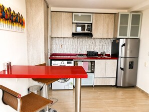 Een kleine keuken met een rode tafel, een magnetron, een fornuis en een koelkast.